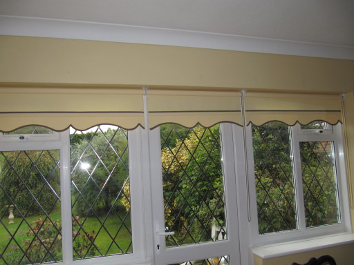 ROLLER BLIND ACROSS FRENCH DOOR AND WINDOWS WITH A SHAPED AND CONTRAST BRAIDED EDGE.