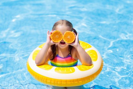Child with oranges as glasses in swimming pool