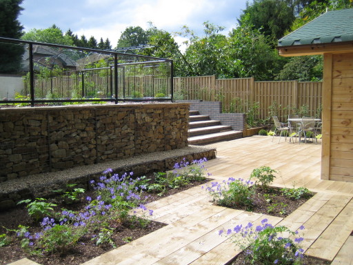 Gabion wall, steel and glass balustrade, composite decking on sloped garden