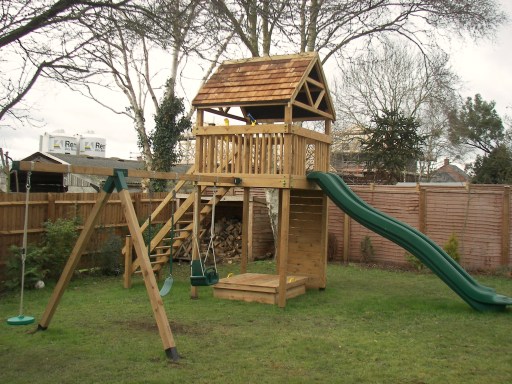 Residential play tower with a red cedar shingle roof, slide, climbing wall, swing arm and sandpit
