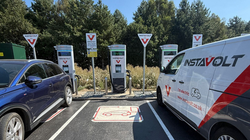A clear view of InstaVolt’s rapid and ultra-rapid chargers in use, located at a tree-lined charging site. The charging bays are clearly marked and show both cars and a branded InstaVolt van plugged in.