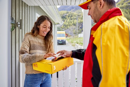 DHL Express courier completing a parcel delivery at a residential porch while the recipient signs electronically on a handheld device.