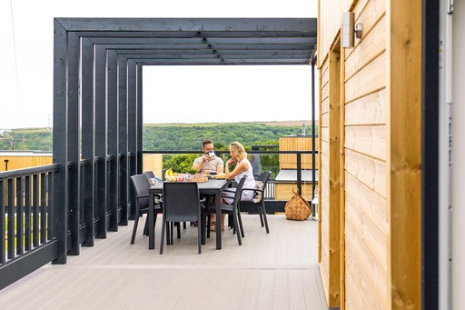 Couple enjoy breakfast on the decking of their Luxury Eco Lodge at Gwel an Mor