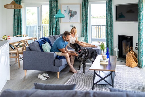 Couple relax in the living area of their pet-friendly lodge with their dog at Gwel an Mor