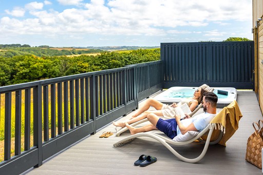 Couple relax on the decking of their Lodge and admire the view of Gwel an Mor