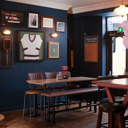 Stylish high table seating area with sports-themed wall decor, creating a relaxed spot for drinks and casual dining.