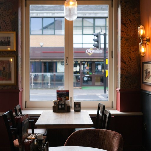 Cosy table for two by a large window, offering a bright and comfortable setting for casual drinks or dining.