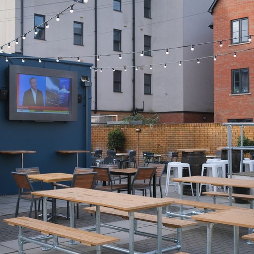 Outdoor seating area with picnic benches and a large screen, perfect for enjoying drinks and live sport outside.