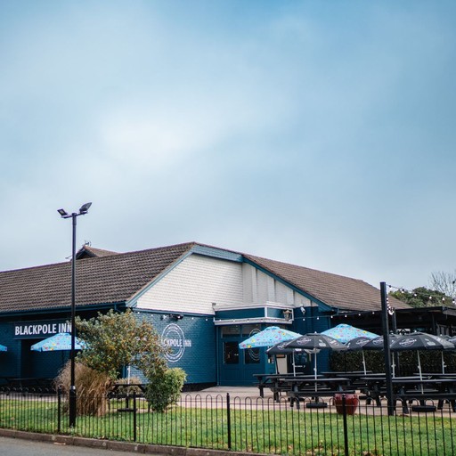 Exterior view of the pub with outdoor seating and branded signage, welcoming guests for drinks and dining.