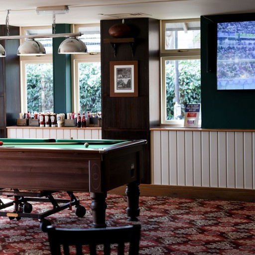 Pool table positioned within a social space alongside a large screen, combining games and live sport viewing.