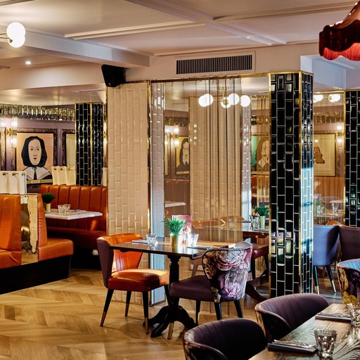 Stylish restaurant interior with velvet chairs, round tables, and portraits on the walls.
