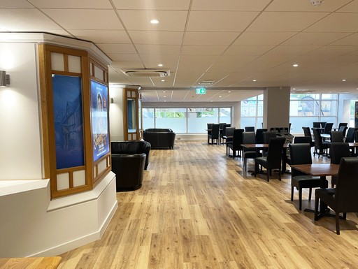 A spacious, modern dining area with wooden floors, black chairs, and large windows.