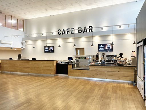 Spacious café bar with wooden counters, menu screens, and a display case on a wooden floor.