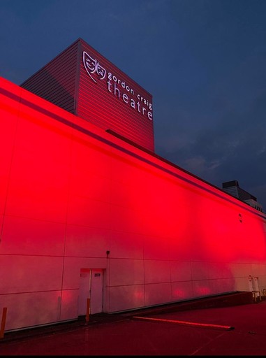 White building of Gordon Craig Theatre lit up with red lights at dusk.