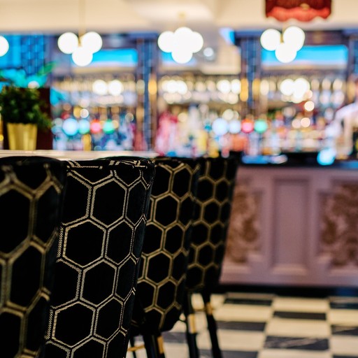 Bar interior with hexagon-patterned chairs, plants, and blurred lights in the background.