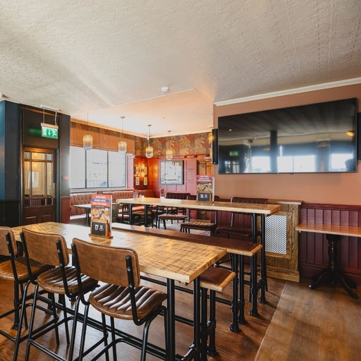 A modern seating area inside The Victoria Park Hotel with high tables and a large TV screen, suited to social drinks and live sport viewing.