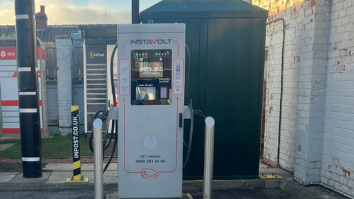 An InstaVolt rapid EV charger located beside InPost and DPD parcel lockers, set against a brick wall in an urban environment.