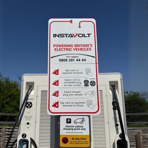 A clear view of the user instructions on an InstaVolt EV charging unit located at McDonald’s Bridgwater Business Park. The signage explains how to use the contactless payment system and select either CCS or CHAdeMO connectors, with a backdrop of blue sky and greenery, enhancing visibility and simplicity for EV drivers.