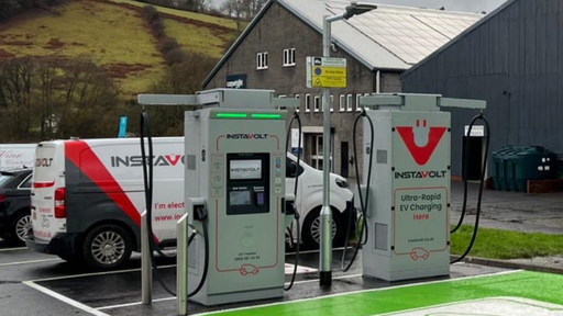 EV charging station in Llanidloes featuring InstaVolt chargers, scenic hill backdrop and branded service van in the background.