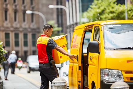 DHL Express courier loading yellow DHL Express boxes into a yellow delivery van on a city street.