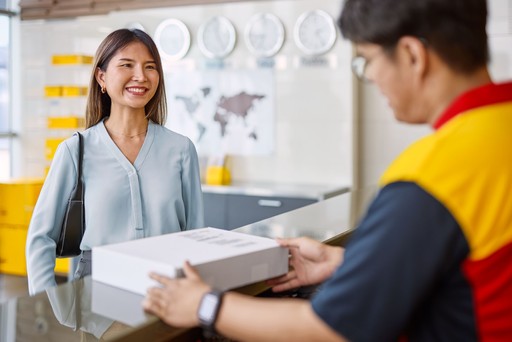Customer receiving a parcel from a DHL Express courier at a service counter inside a DHL Express Service Point.