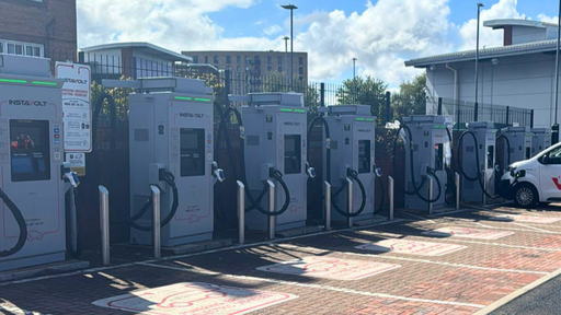 This side-angle photo captures multiple InstaVolt chargers in a row, with clear EV-only markings and brick paving, set against a bright blue sky at the Dunelm site in Birmingham.