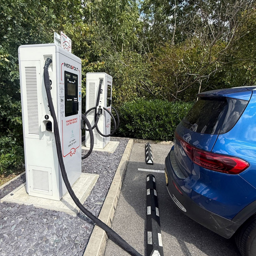 Close-up of a blue electric vehicle charging at InstaVolt EV points near woodland.