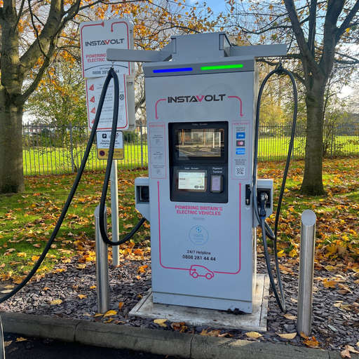 A close-up of an InstaVolt charger in a well-lit daytime setting, with clear signage and autumn leaves scattered around, showcasing ease of use.