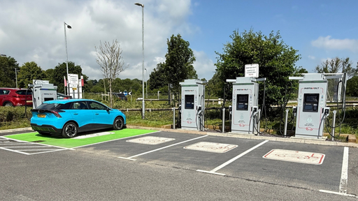 This wide-angle shot showcases multiple InstaVolt ultra rapid chargers at the Wincanton A303 site, with a blue EV actively charging. The site includes several clearly marked charging bays, surrounded by greenery and adjacent to the A303 for convenient access.