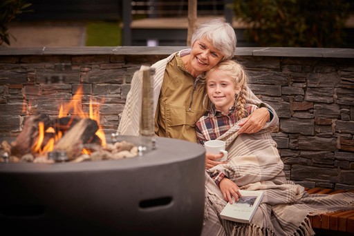 Grandmother sits with her granddaughter by a Fire Pit next to their Forest Pod at Stratheck