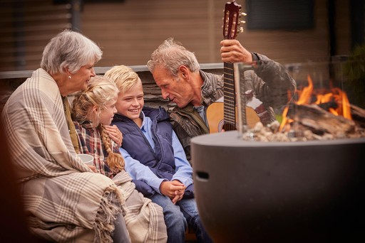Grandparents sits with their grandchildren by a Fire Pit next to their Forest Pod at Stratheck