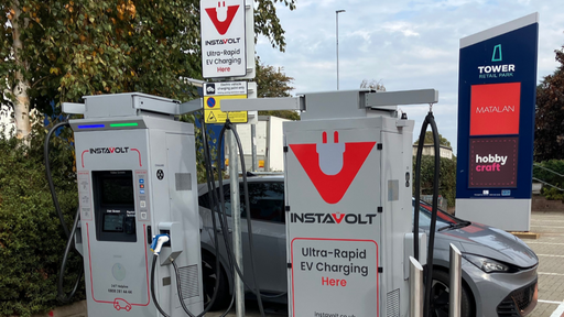 Two InstaVolt ultra-rapid chargers next to the Tower Retail Park sign featuring Matalan and Hobbycraft, with an electric vehicle plugged in.