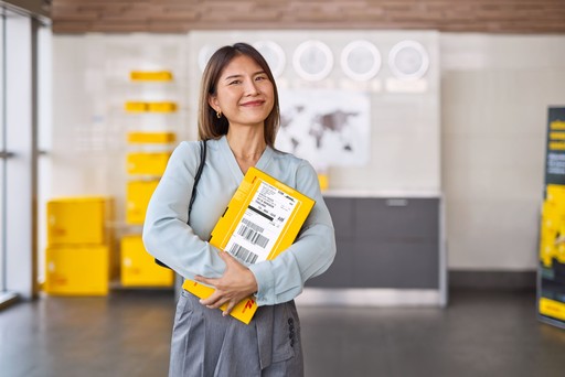 Person holding a yellow DHL Express parcel with a visible shipping label inside a DHL Express service centre.