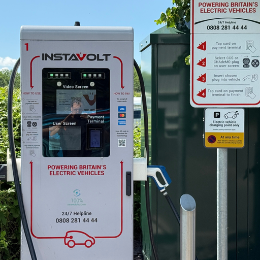 Detailed close-up of an InstaVolt ultra rapid charger at Costa Coffee Ilminster, highlighting the touchscreen interface, CCS and CHAdeMO connector options, and on-site usage guidance. Also visible is an instruction signpost with helpline info and a clearly marked EV-only parking notice.