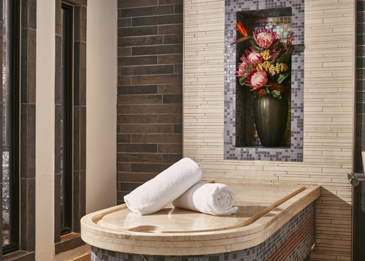 A stack of fresh, white towels sits neatly on the table, ready for use. The room is adorned with elegant, dark wood paneling and a beautiful floral arrangement displayed in a niche. The overall atmosphere is calming and inviting, perfect for a spa experience.