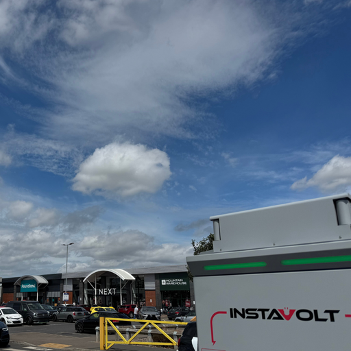 An InstaVolt charger is seen in the foreground, with a wide view of Gallagher Retail Park’s retail offering including Next, Mountain Warehouse, and Poundland.
