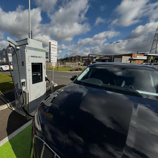A black EV is connected to an InstaVolt charger at McDonald’s Fairhill, Bedford. The McDonald’s restaurant is clearly visible behind the charging area.