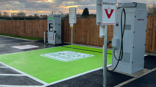 InstaVolt ultra-rapid EV chargers with visible "Rapid Charge Here" signage and freshly marked charging bays, captured under a dramatic evening sky.