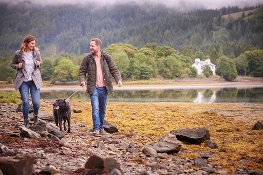 Couple stroll with their dog through the grounds of Drimsynie Estate