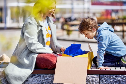 A person and a child sitting outdoors, opening a yellow DHL Express Box with blue tissue paper inside.