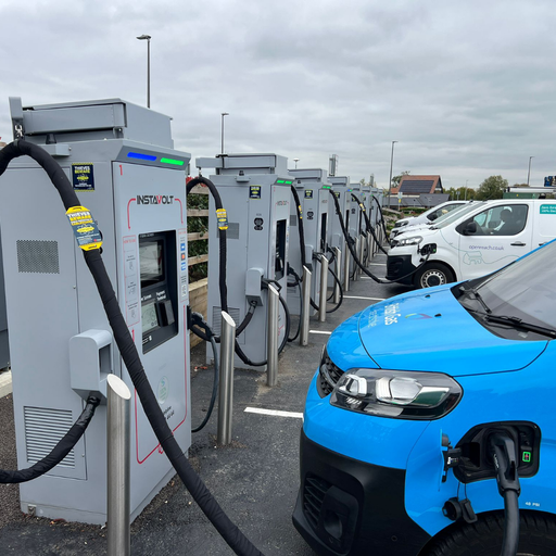A row of InstaVolt ultra-rapid chargers actively powering electric vans from companies like Openreach and British Gas at a public charging site.
