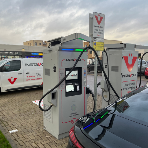 The photo captures an EV charging at an InstaVolt ultra-rapid charger in Berryfields, Aylesbury. An InstaVolt-branded van and nearby shops, Berryfields Fish Bar, are visible, emphasising service presence and local convenience.