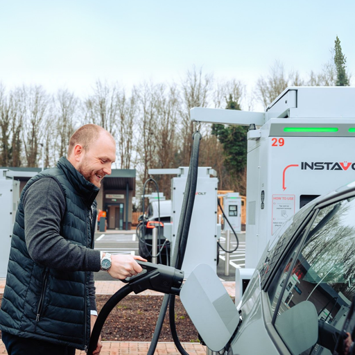 A man charging his electric car at an InstaVolt station, with multiple chargers and woodland scenery in the background.