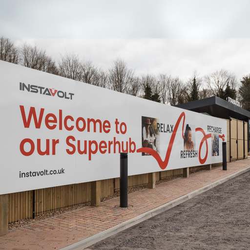 A close-up of the InstaVolt superhub welcome sign with the tagline “Relax, Refresh, Recharge”, situated beside a landscaped path.