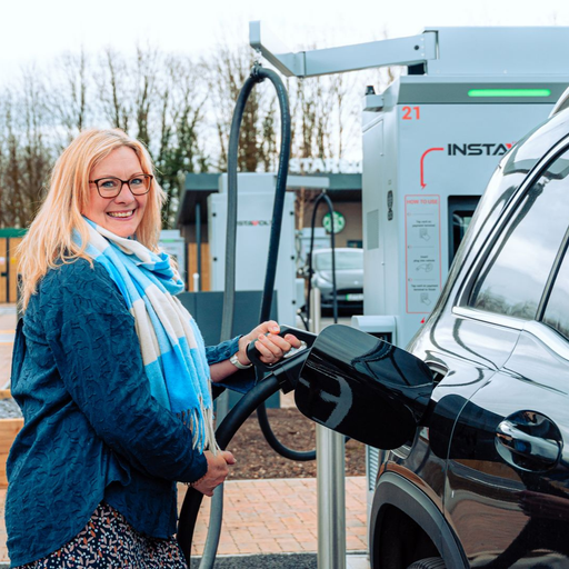 A woman smiling at the camera while charging her SUV at an InstaVolt charging station, with visible branding and a Starbucks café in the background.