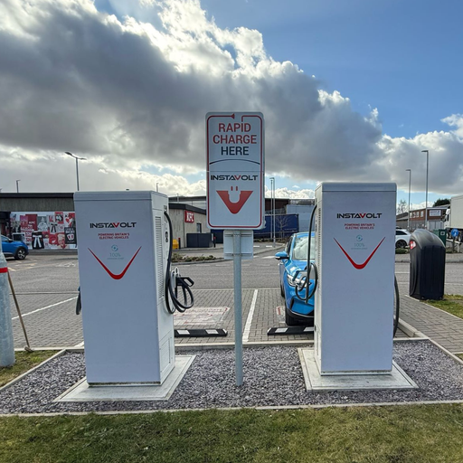 Rear view of two InstaVolt chargers at Rugeley’s Leathermill Lane site, with a blue EV parked and KFC visible behind the chargers.