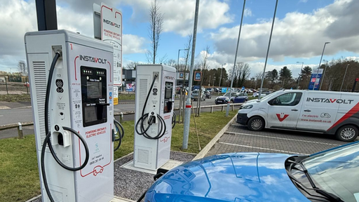 A blue electric vehicle charges at InstaVolt’s Rugeley location, with Aldi signage in the background and an InstaVolt service van parked nearby.