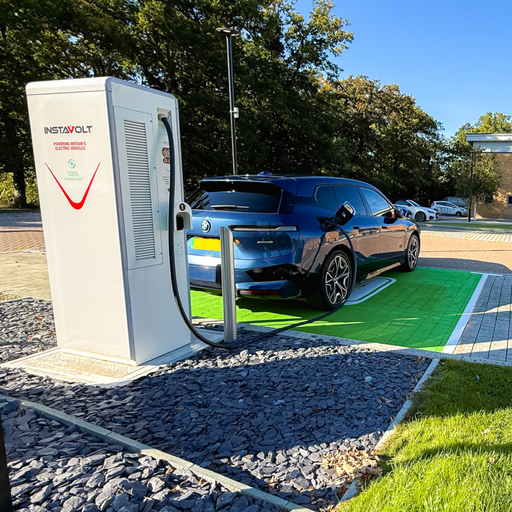 Close-up of an EV charging cable connected to a BMW electric vehicle with a Fitness First gym visible in the background.