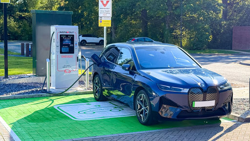 A BMW EV is plugged into an InstaVolt ultra rapid charger in a dedicated green EV bay.
