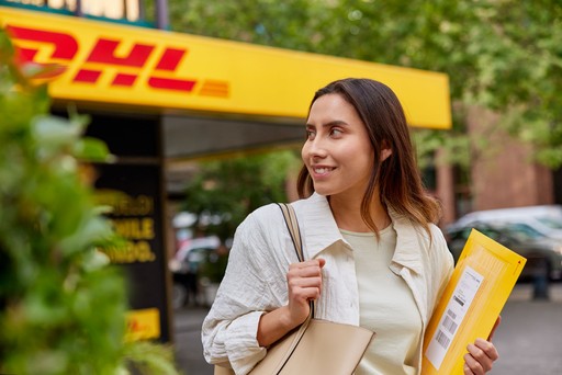 Customer holding a yellow DHL envelope outside a DHL Express Service Point location.